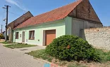 Světle zelený rodinný dům s červenou střechou a garáží u ulice.